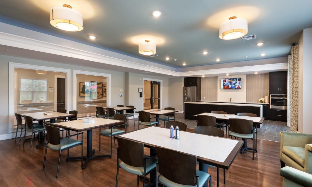 A modern dining area with neatly arranged tables and chairs, featuring stylish lighting and a kitchen setup in the background.