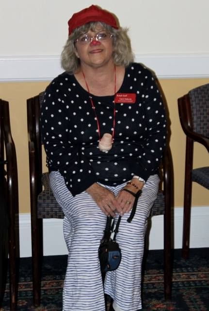 A woman sitting indoors, wearing a polka dot shirt and striped pants, holding a camera.