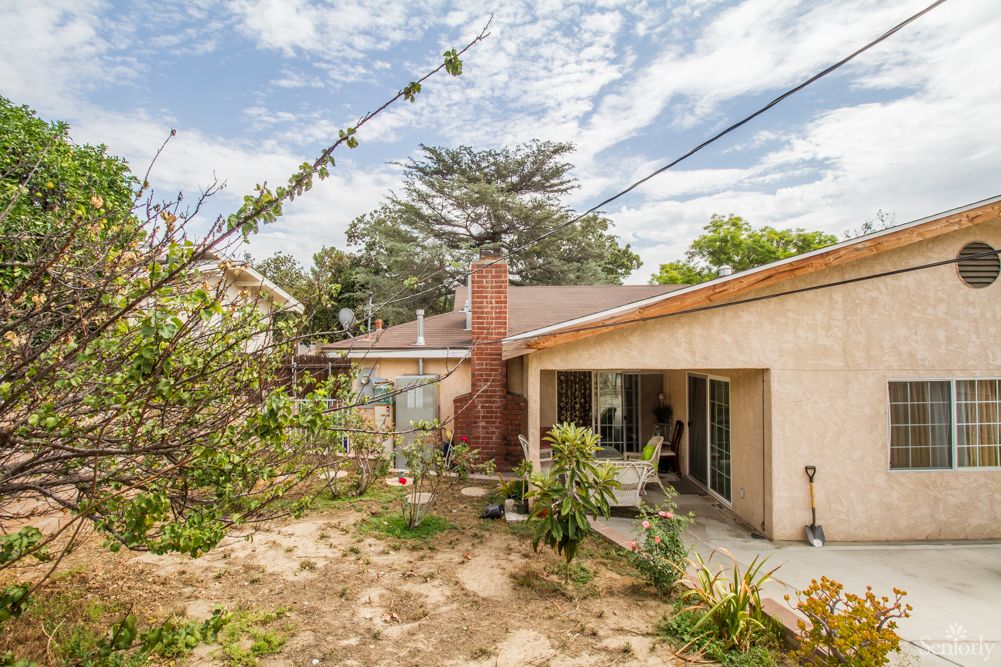 A backyard view of a house with a patio and garden area under a partly cloudy sky.