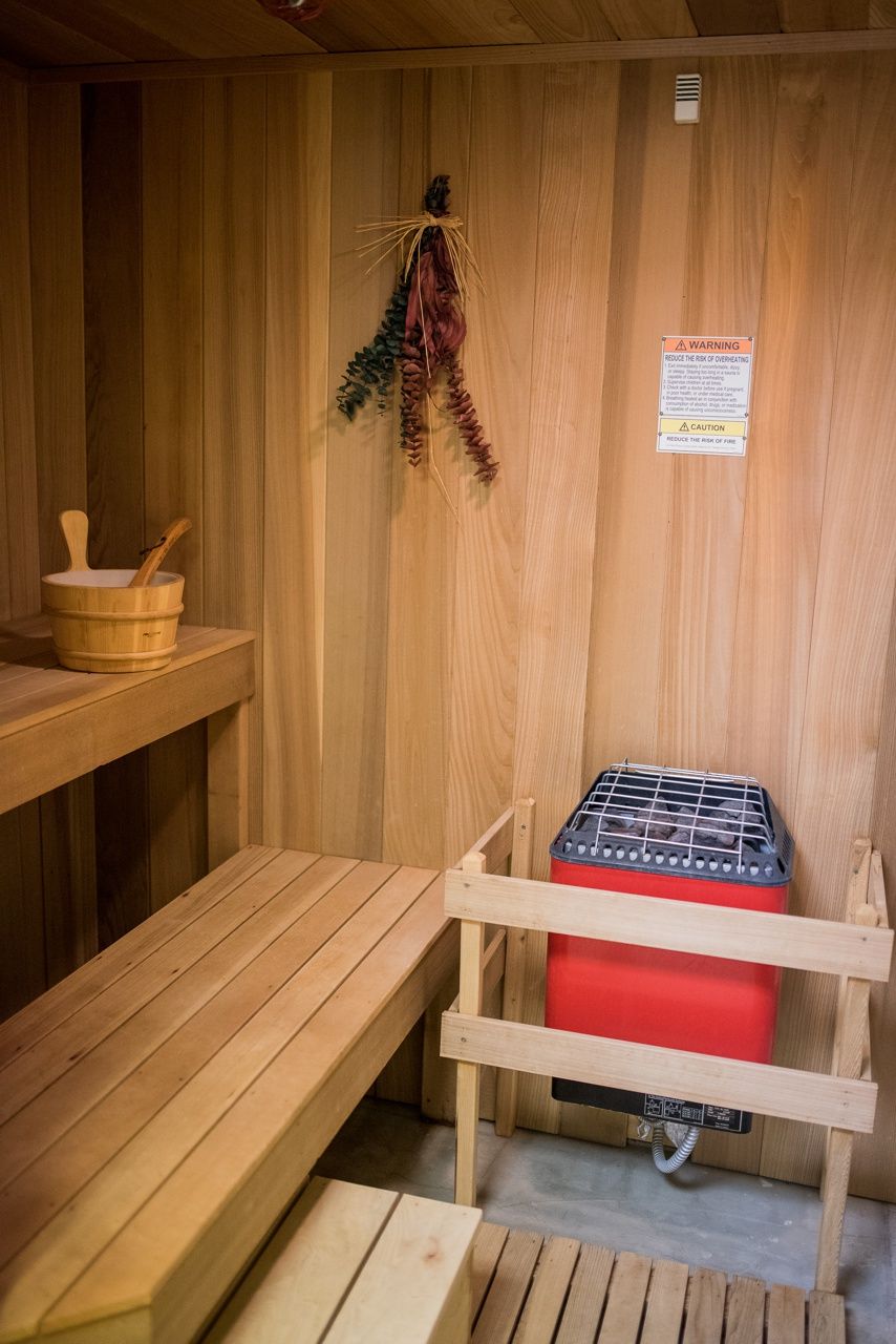 A cozy wooden sauna with a bench, bucket, and heating element.