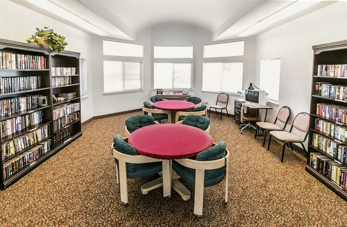 A comfortable library room with round tables, chairs, a bookshelf, and a computer.