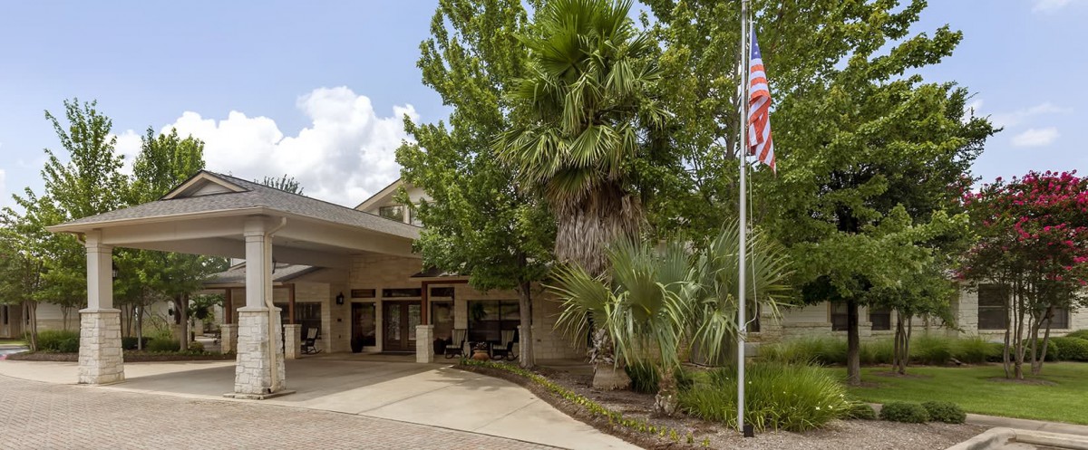 A building entrance surrounded by lush greenery and an American flag.