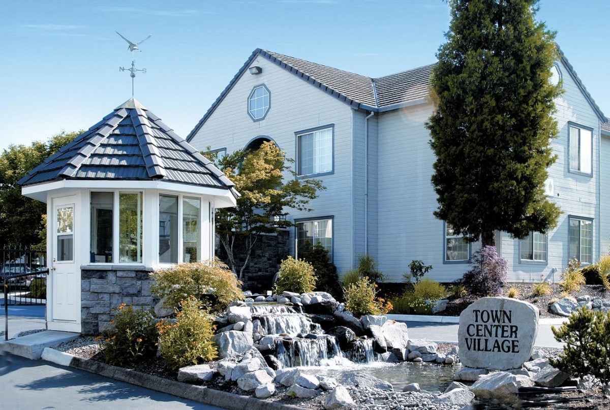 A scenic view of a quaint village setting featuring a fountain, gazebo, and landscaped garden.