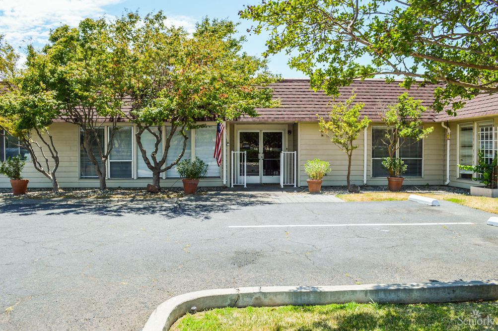 Small building with trees and a parking lot in front.