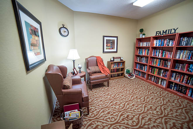 A cozy office space with armchairs, a bookshelf filled with books, and warm lighting.