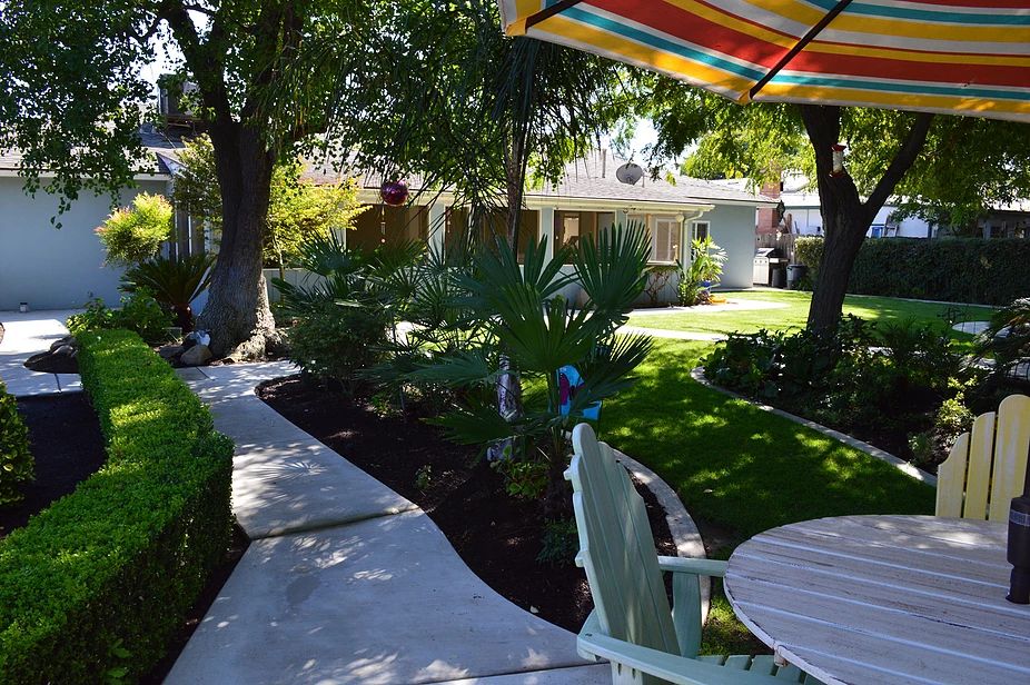 A serene backyard garden with a patio set under a colorful umbrella.