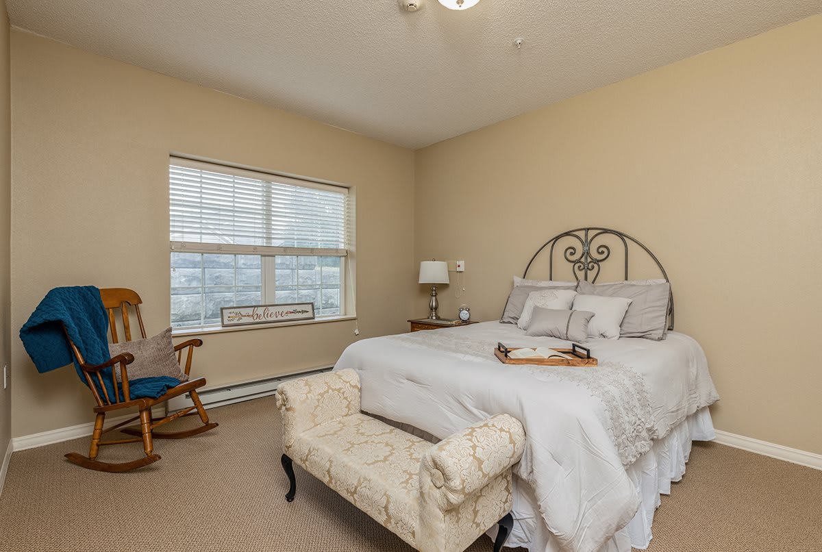 A cozy bedroom with a large bed, ornate headboard, and a rocking chair by the window.