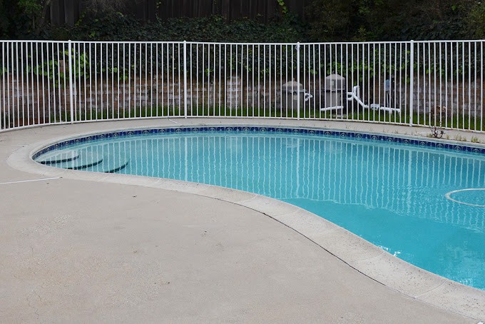 An outdoor swimming pool with a surrounding fence and nearby lounge chairs.