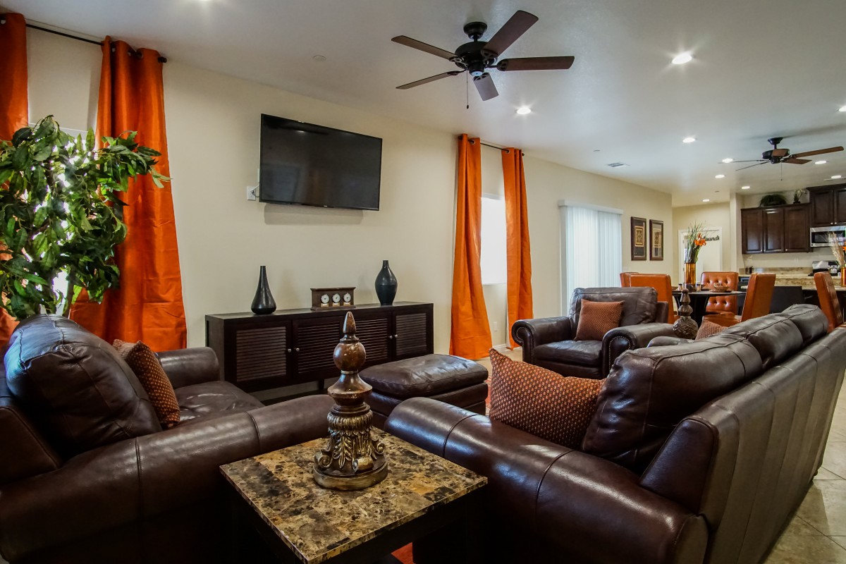 A modern living room featuring leather sofas, a television, and bright orange curtains.