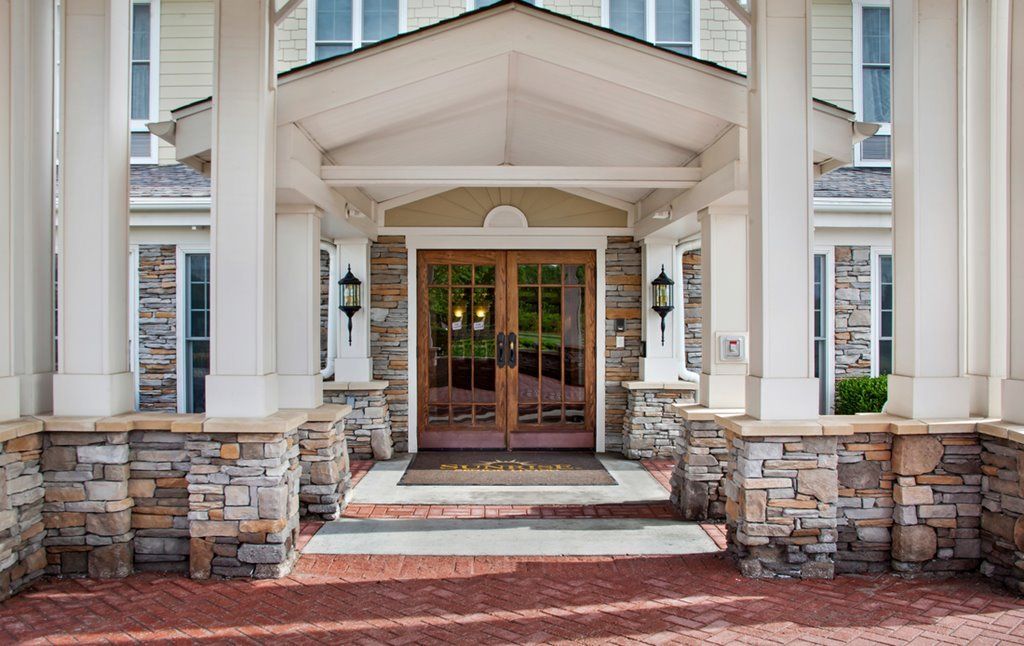 A welcoming building entrance featuring stone columns, a brick pathway, and double wooden doors.
