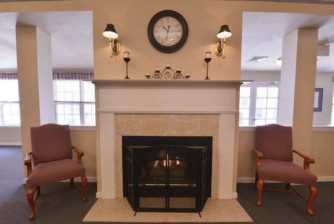 A cozy living room with a fireplace and armchairs, featuring a clock above the mantel.