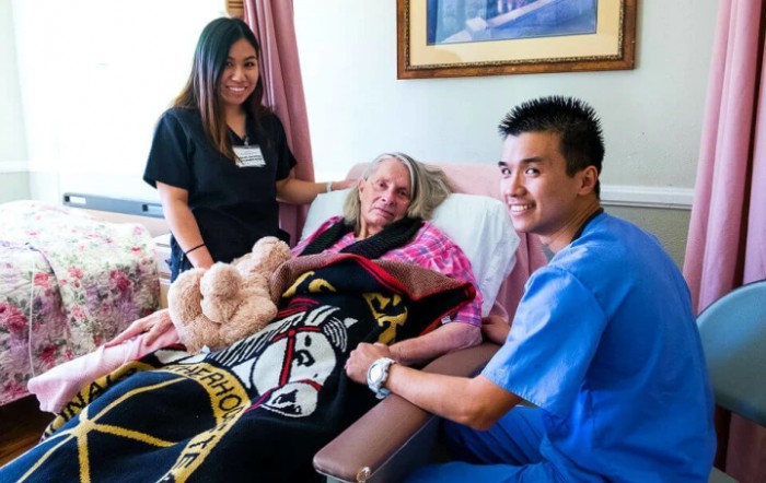 Medical staff assisting an elderly patient in a hospital room.