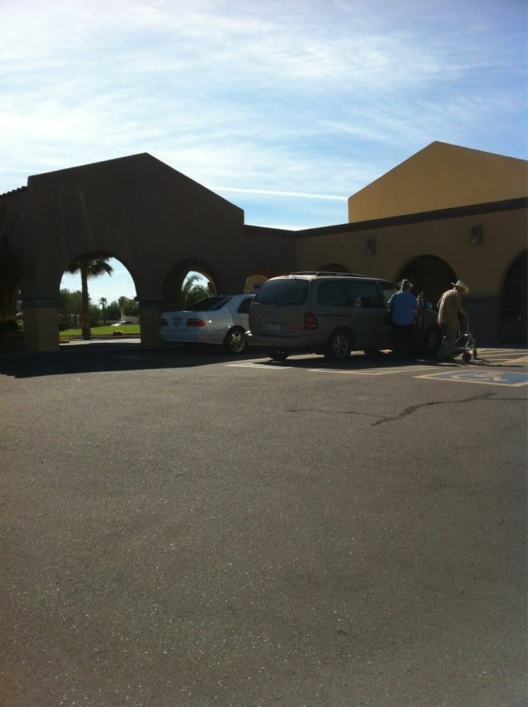 A parking area in front of a building with arched entrances under a clear blue sky.