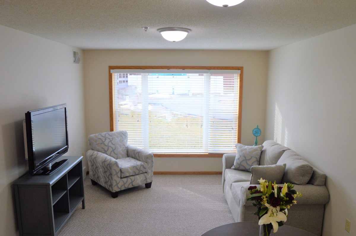 A cozy living room with a sofa, armchair, and large window providing ample natural light.
