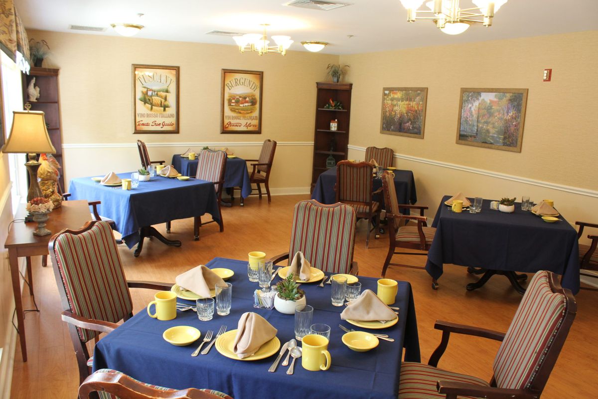A neatly arranged dining room with tables set for a meal, featuring blue tablecloths and yellow dishware.