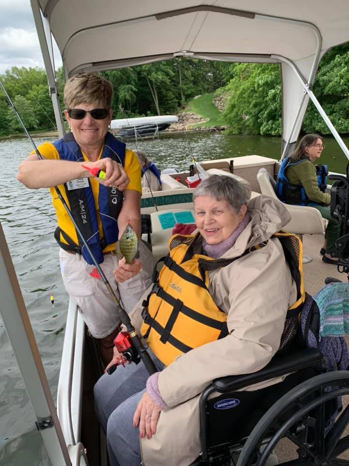 A group of people enjoying a fishing trip on a lake, with one person in a wheelchair holding their catch alongside a companion.