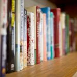 A row of books on a wooden bookshelf with some spines blurred.