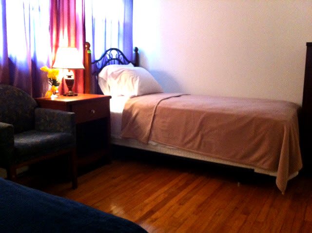 A cozy bedroom with a single bed, nightstand, and a lamp by the window.