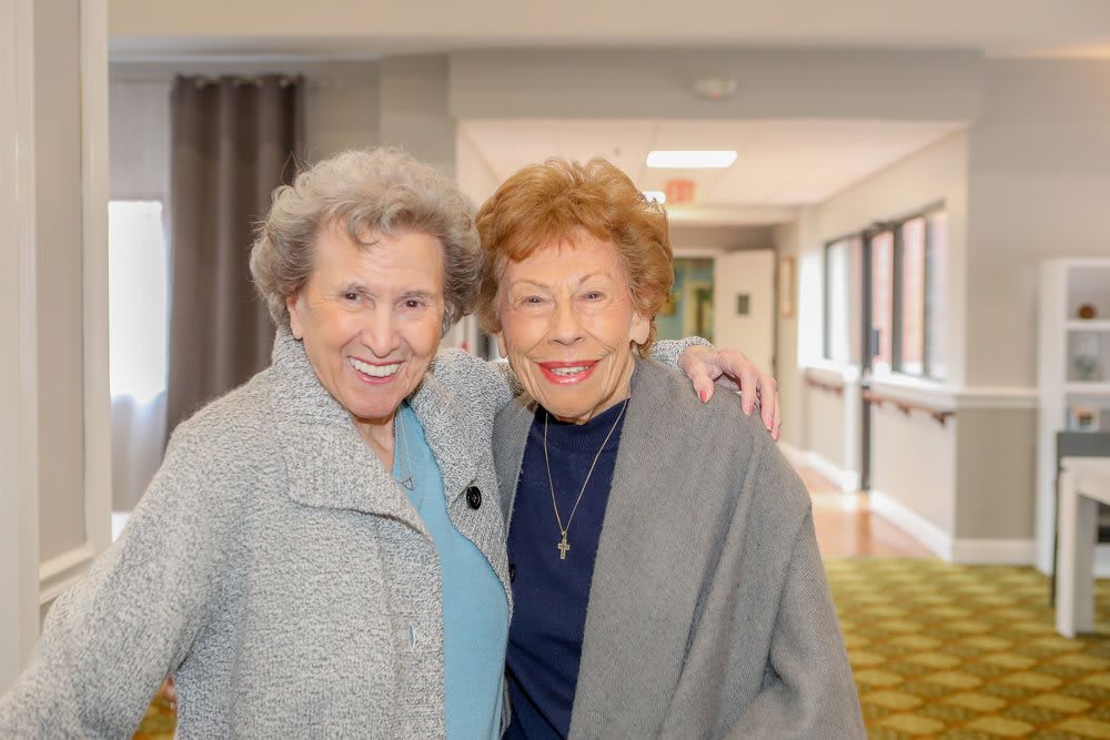 Two elderly women smiling and posing together in a hallway.