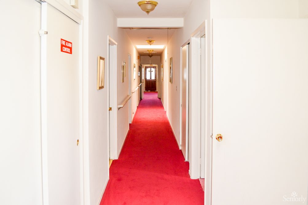A narrow hallway with a red carpet, lined with doors on both sides and overhead lighting.