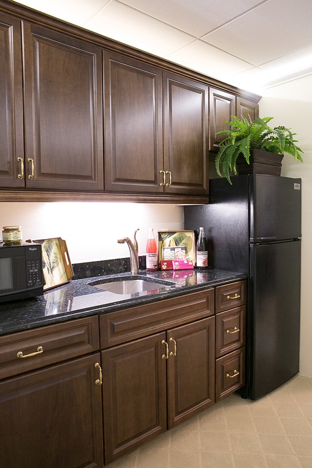 A modern kitchen with dark wooden cabinets and a black refrigerator, featuring a sleek countertop with a sink and a microwave.