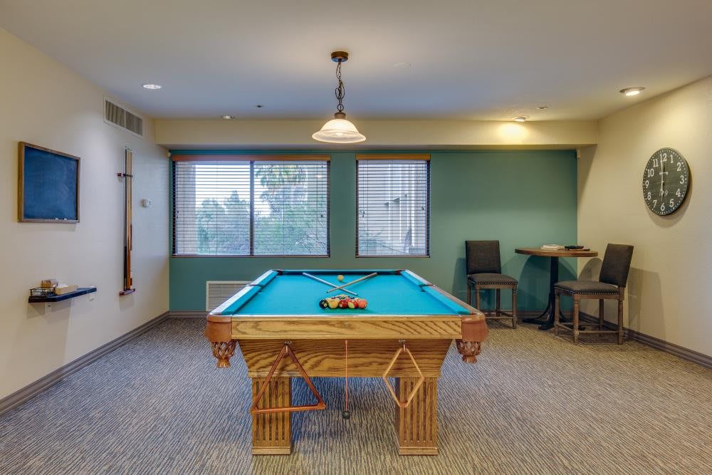A cozy game room featuring a pool table under a hanging light, with seating and large windows providing outside views.