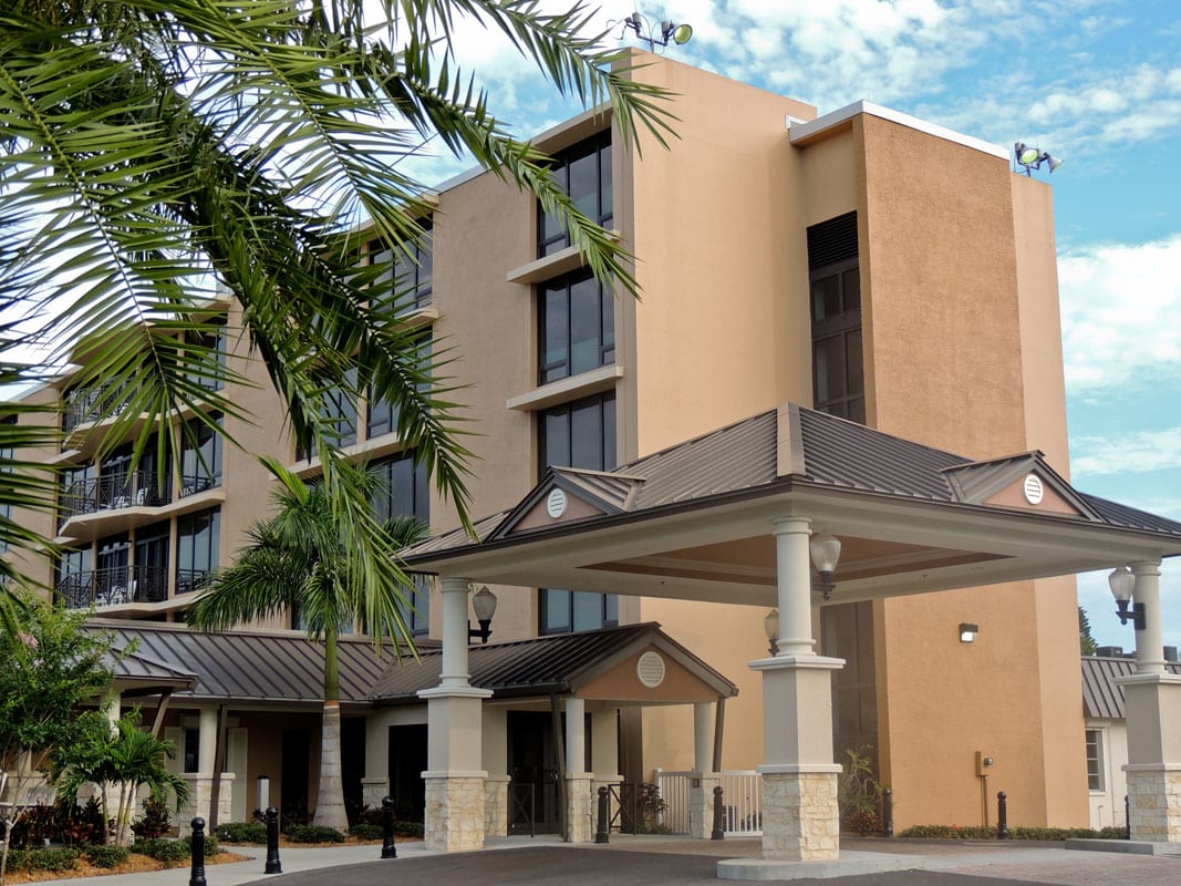 A modern hotel building with palm trees and a covered entrance.