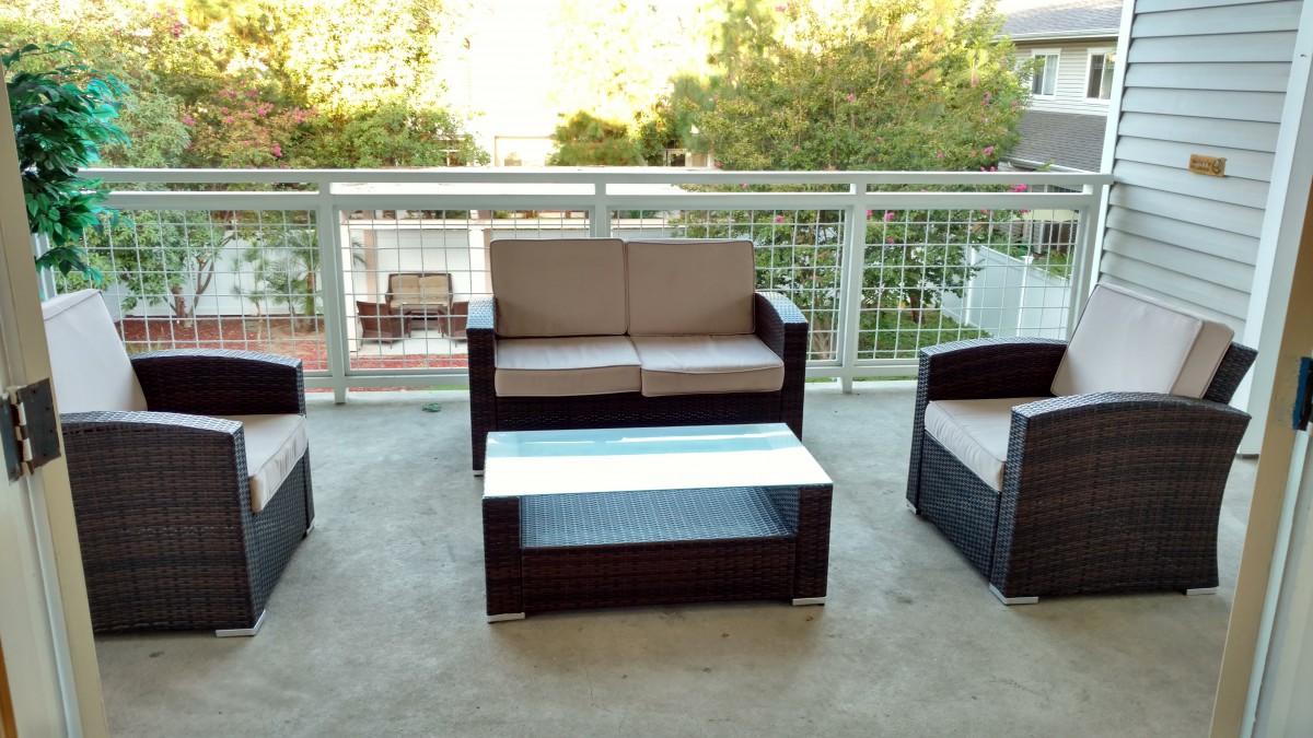 A cozy outdoor patio set on a balcony, featuring a loveseat, two chairs, and a coffee table.