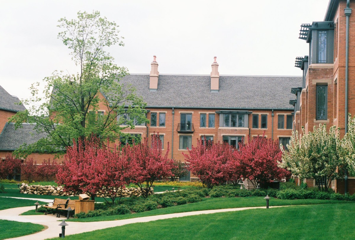 A picturesque scene featuring a brick building surrounded by blooming trees and well-maintained gardens.