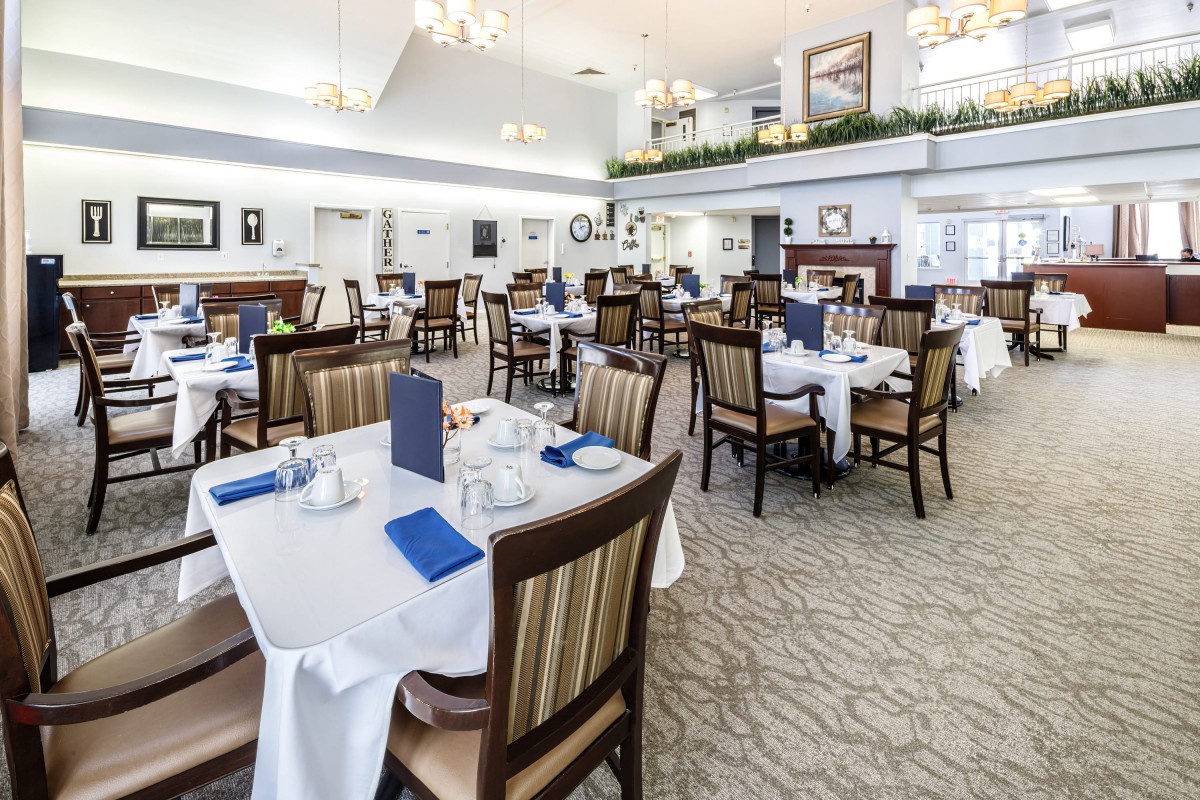 A spacious restaurant dining area with neatly arranged tables and chairs, featuring white tablecloths and blue menus.