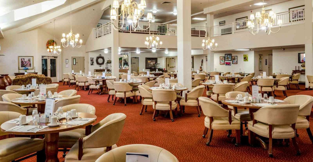 A spacious restaurant dining area with elegant chandeliers and neatly arranged tables and chairs.