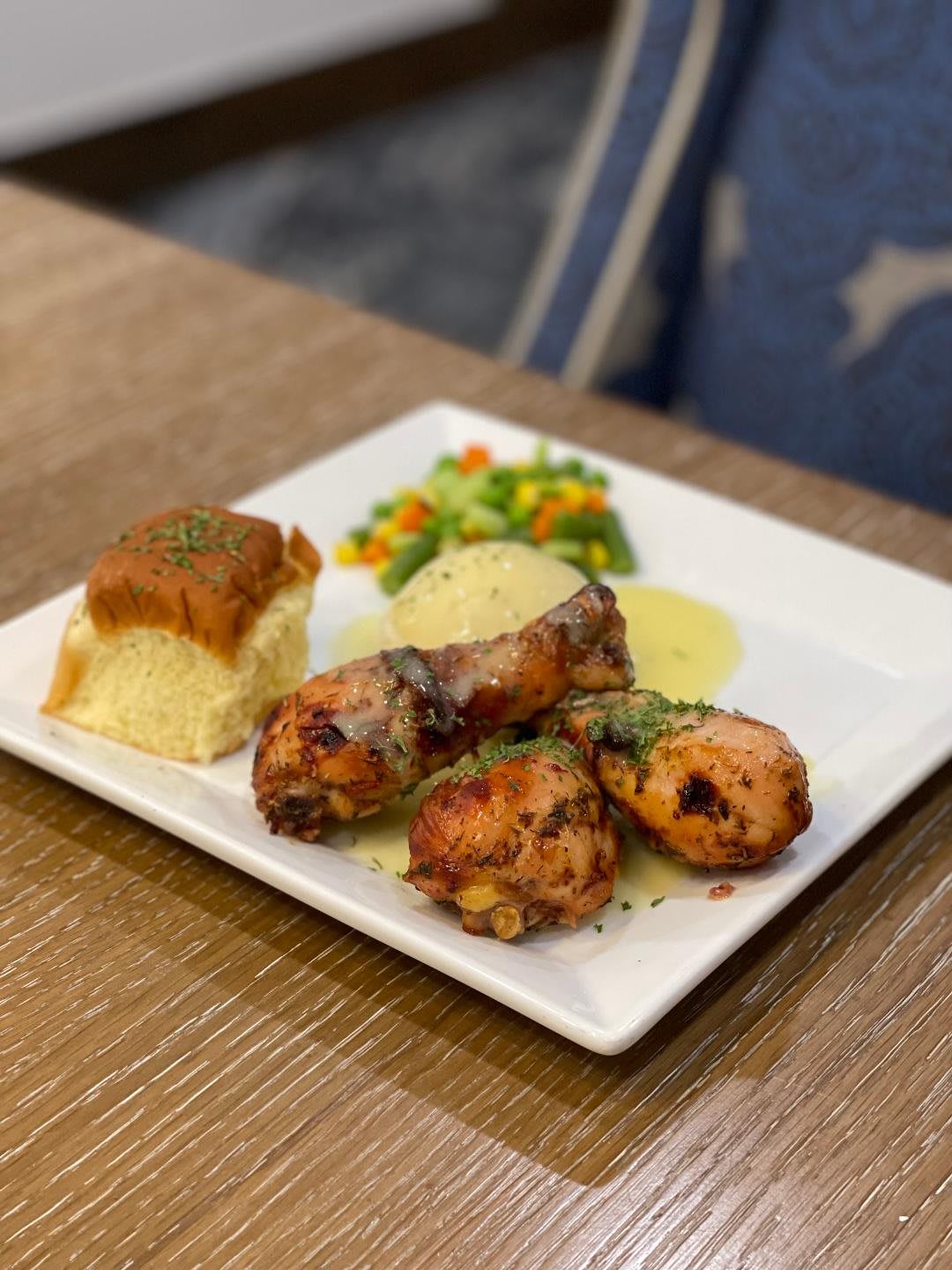 A plate of grilled chicken served with vegetables and a side of bread.