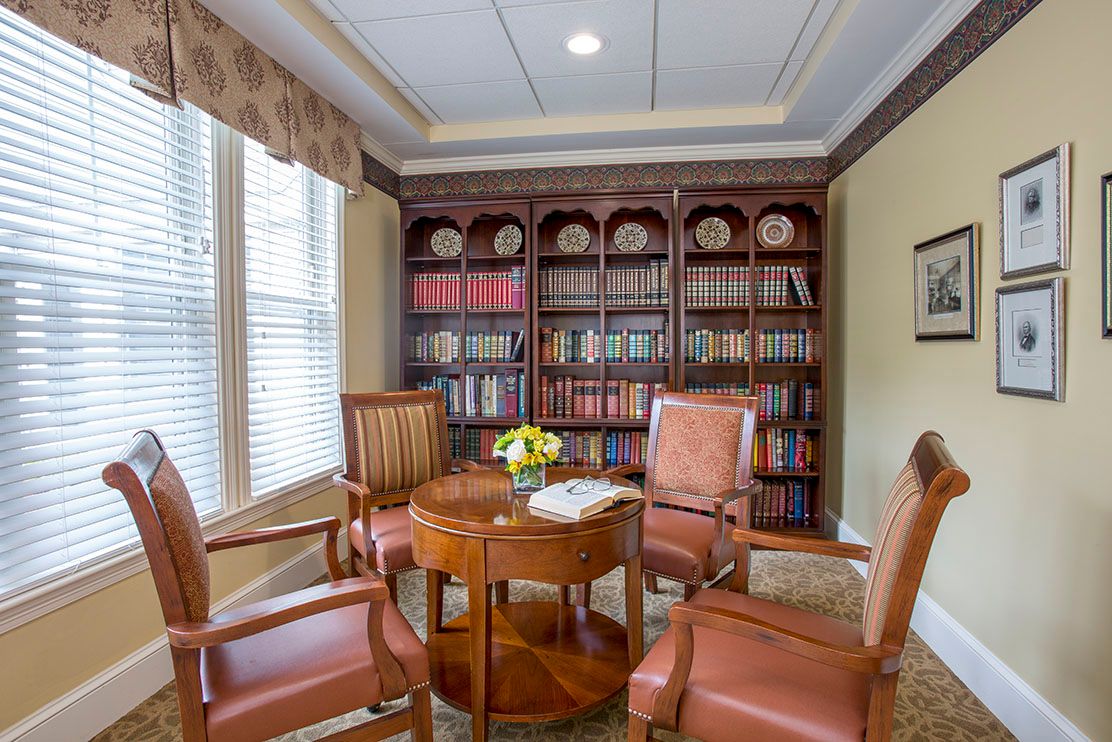 A cozy library corner with a wooden table surrounded by four chairs and a bookshelf filled with books.