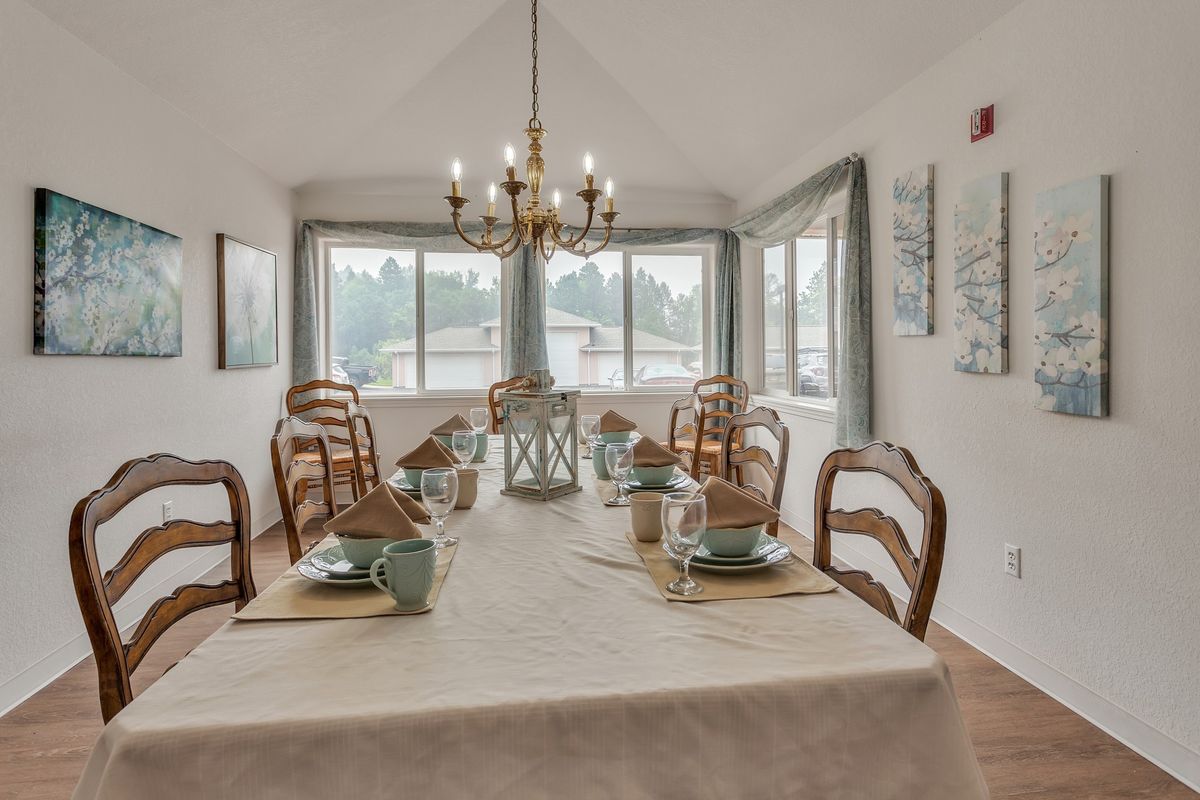 A beautifully set dining room with a large table, elegant chandelier, and ample natural light from surrounding windows.