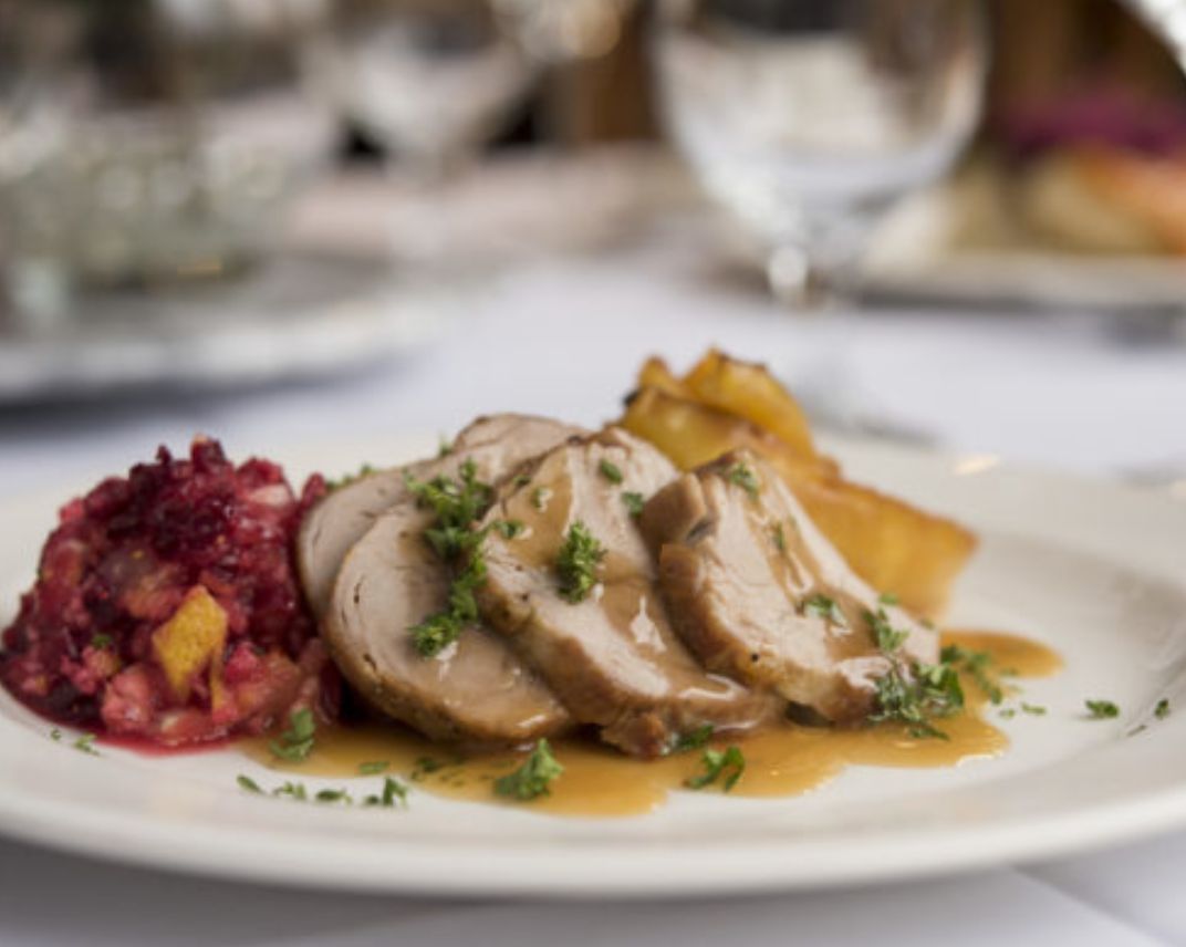 A gourmet plate featuring slices of chicken with sauce, accompanied by a side of vegetables.