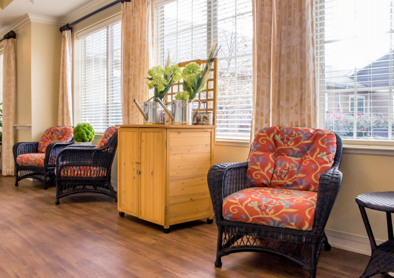 A cozy living room with wicker armchairs featuring patterned cushions, a wooden cabinet, and large windows with curtains.