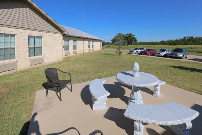 A patio with stone furniture and a view of a grassy area next to a building.