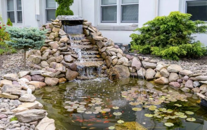 A garden pond with a small waterfall surrounded by rocks and greenery.