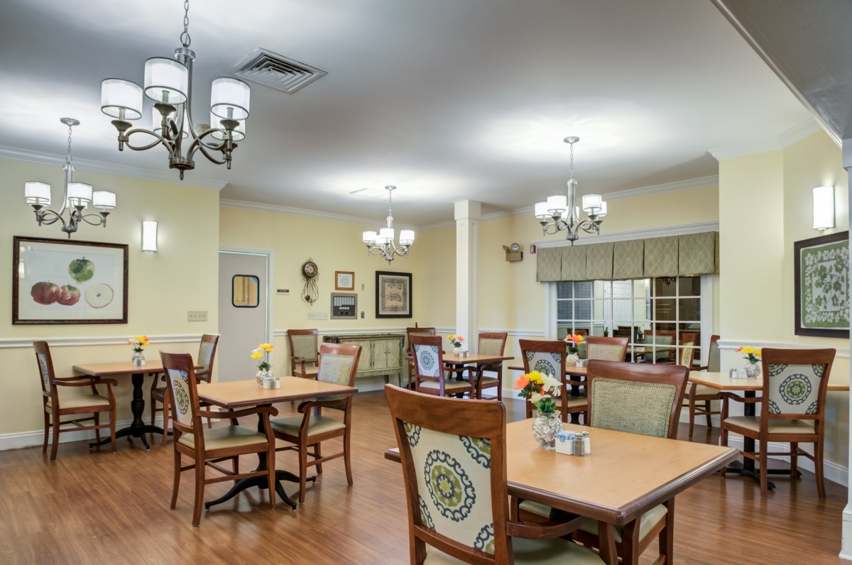 A well-lit dining room with multiple tables and chairs arranged neatly, adorned with chandeliers and interior decorations.