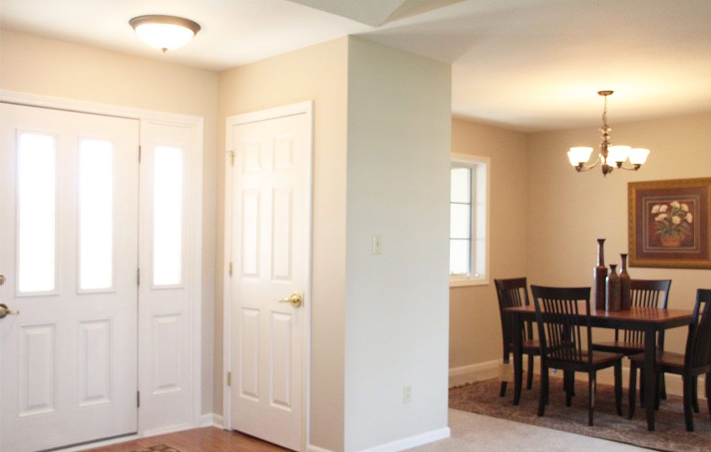 A well-lit entryway leading into a dining area with furniture and windows.