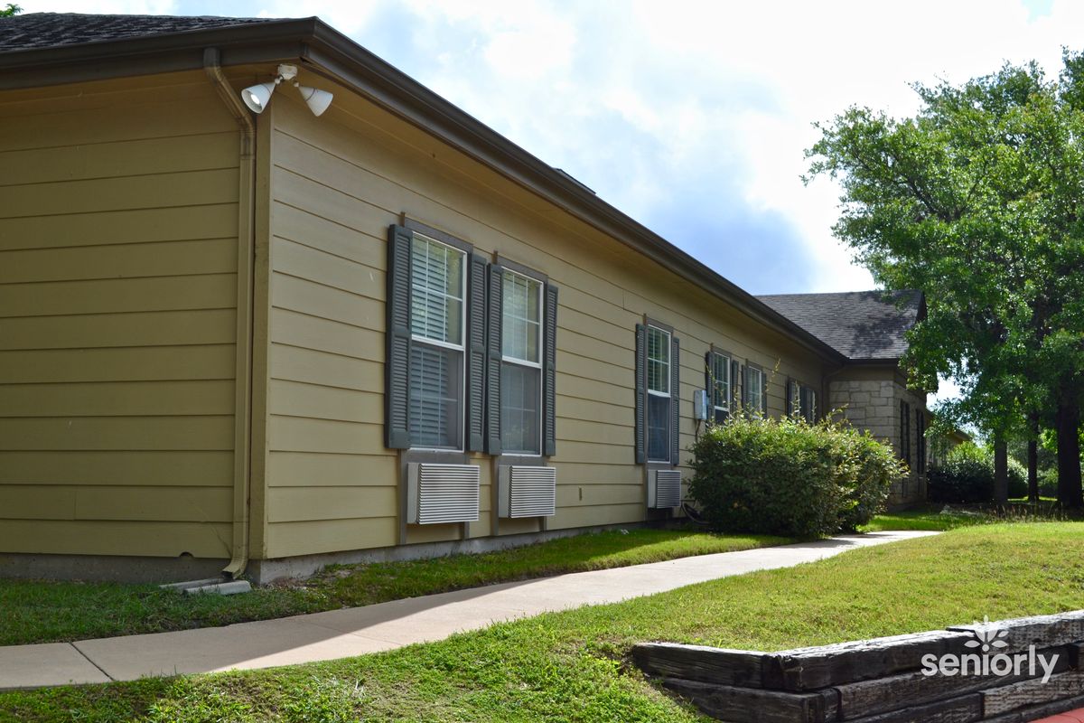 A single-story building with yellow siding, multiple windows, and surrounding greenery.