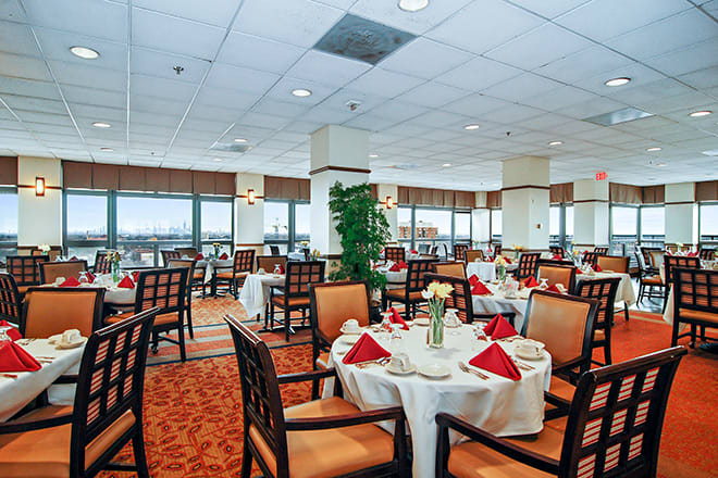 An elegant restaurant dining area with neatly arranged tables and chairs, featuring red napkins and a bright atmosphere.