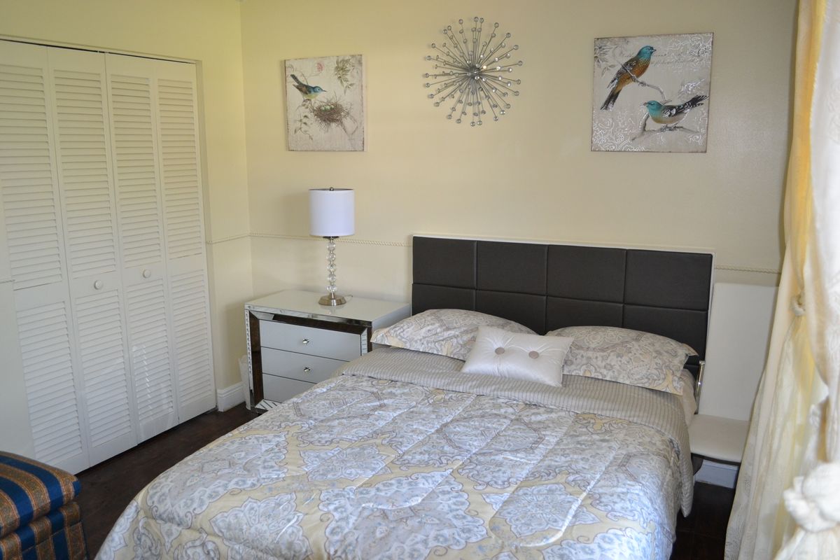 A cozy bedroom with a neatly made bed, wall art, and a lamp on the nightstand.