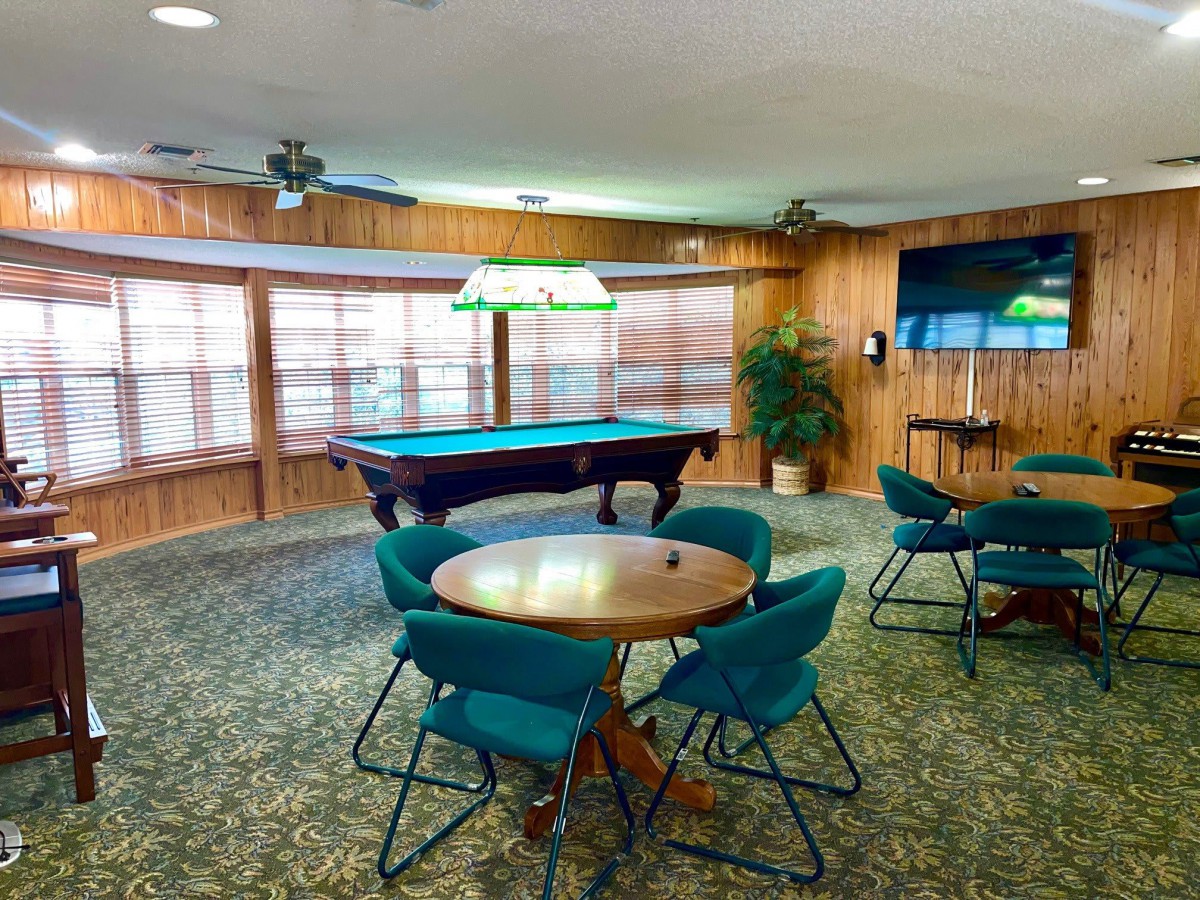 A cozy game room featuring a pool table and seating area adorned with green chairs and hanging lights.