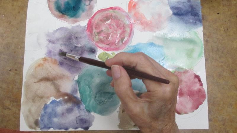 A person painting with watercolors, using a brush to create colorful abstract patterns.