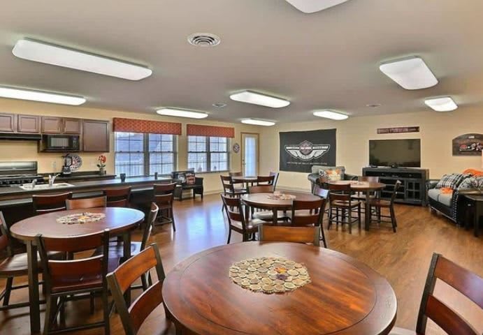 A well-lit community room with multiple tables and chairs, featuring a television and decorative elements.