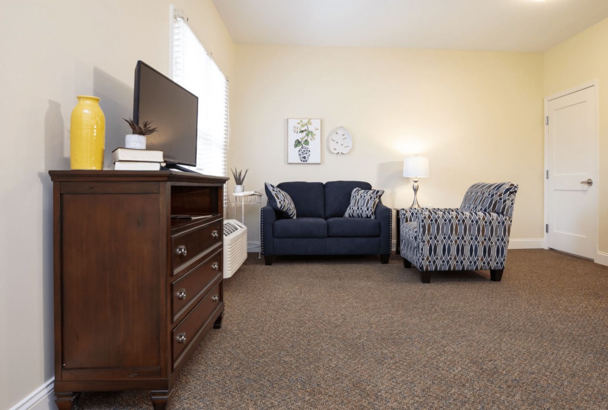 A cozy living room with a sofa, armchair, television, and dresser.