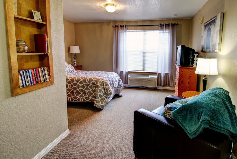 A cozy bedroom interior with a bed, armchair, and a TV near the window.