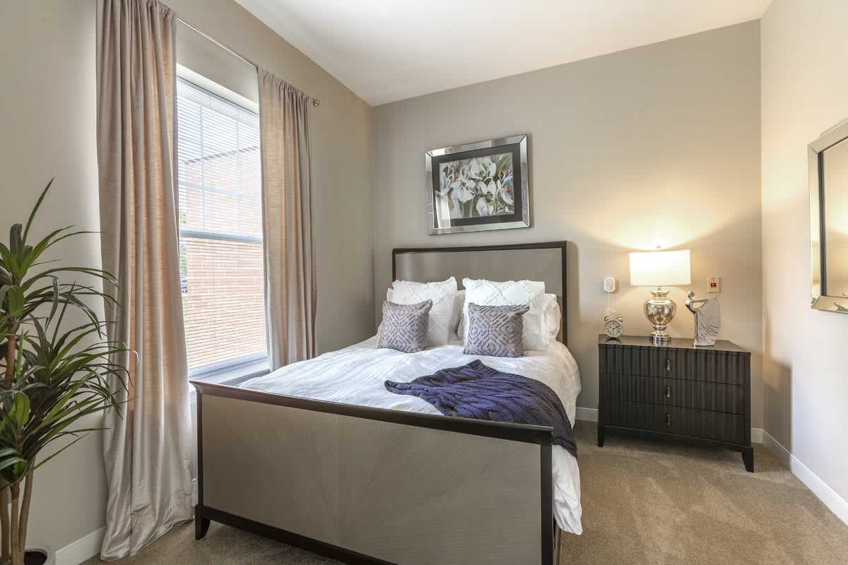 A modern bedroom with neutral tones, featuring a comfortable bed, decorative pillows, and a side table with a lamp.