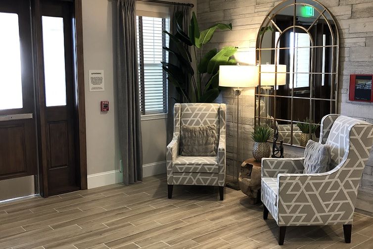 A cozy living room setup with patterned chairs, a standing lamp, and decorative elements like a mirror and plants.